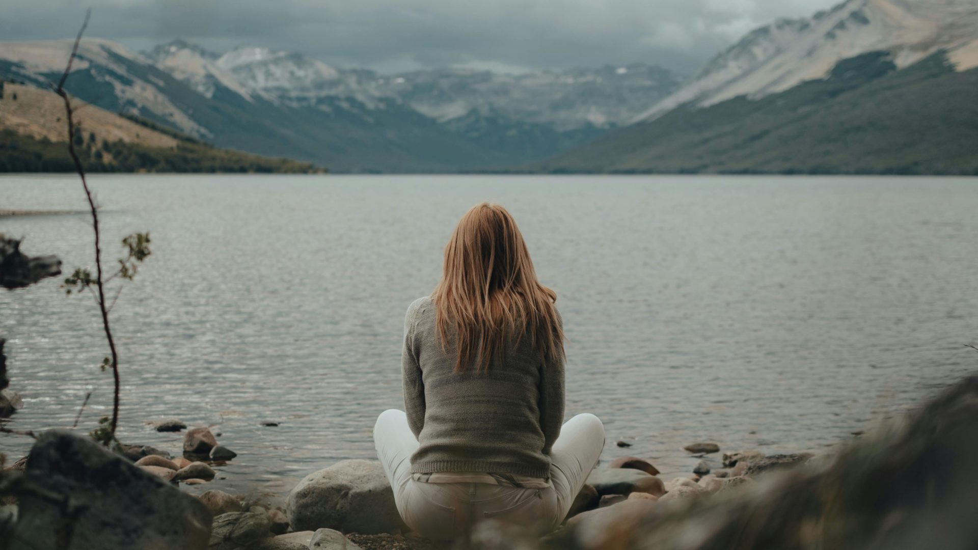 A person sits by a mountain lake, finding peace and solitude in nature's embrace.